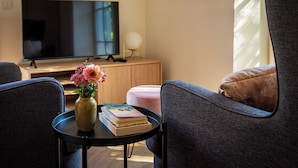 Ein Wohnzimmer mit Fernseher, Blumen in einer Vase, einem Bücherstapel und zwei Stühlen.