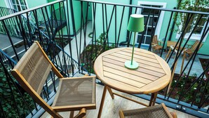 Un balcone con un tavolo di legno rotondo e due sedie, una lampada da terra verde e vista su un edificio verde con una scala.