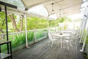 Un patio al aire libre con mesas y sillas, un cerramiento de vidrio y vista a la vegetación.