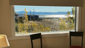 Ein Schlafzimmer mit großem Fenster, zwei Stühlen, einem Bett und einer Lampe.