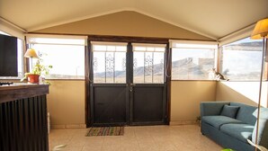 Ein Zimmer mit einer schwarzen Tür, einem blauen Sofa, einem Fernseher und Blick auf eine gebirgige Landschaft.