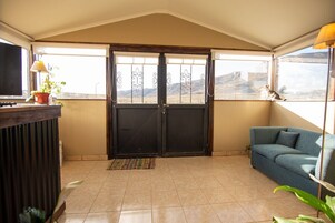 Ein Zimmer mit einer schwarzen Tür, einem blauen Sofa, einem Fernseher und Blick auf eine gebirgige Landschaft.