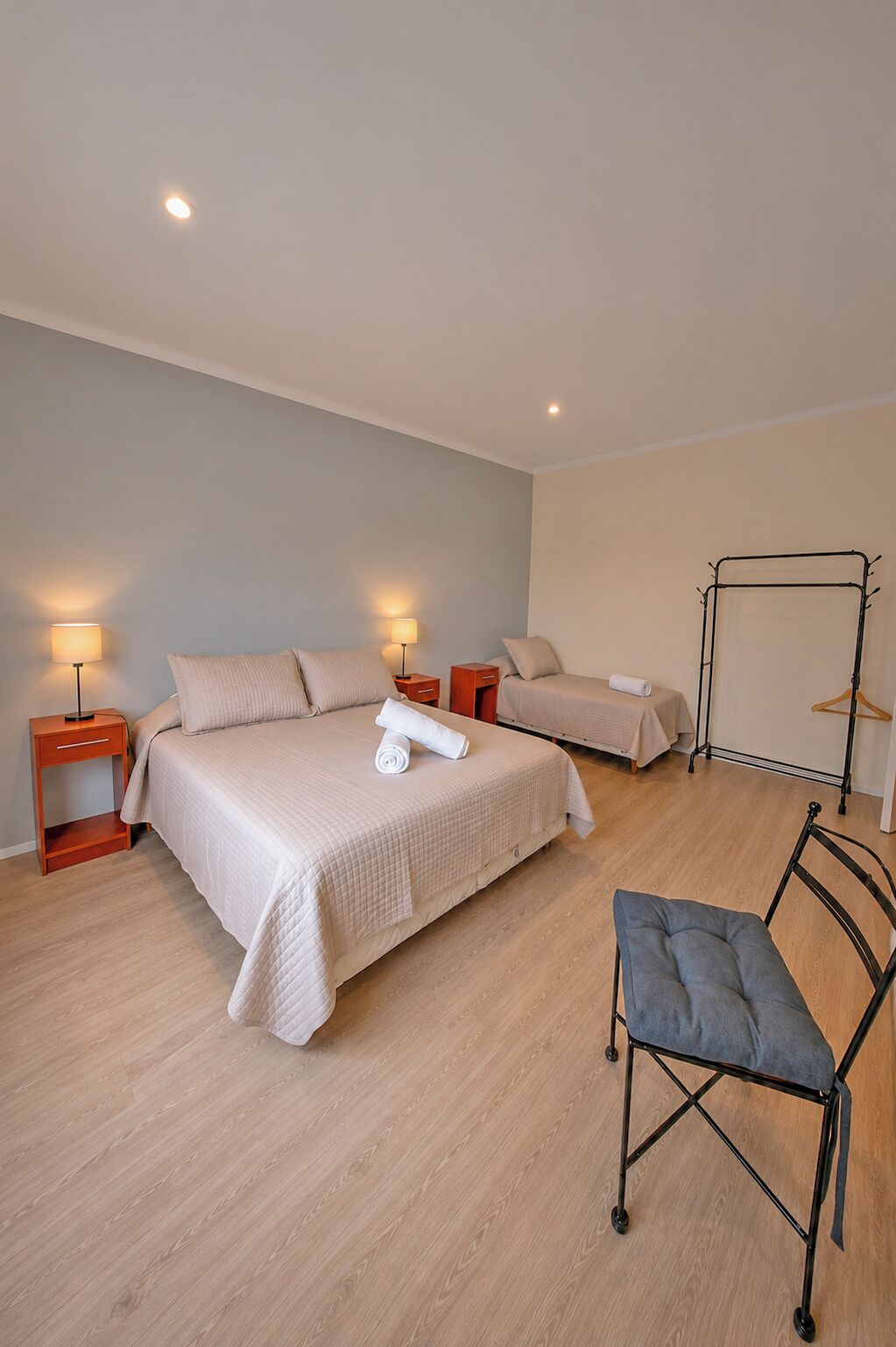 Habitación de hotel con dos camas, una silla, mesitas de noche y un perchero.
