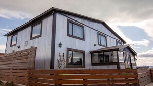 Ein zweistöckiges Gebäude mit Wellblechfassade, zahlreichen Fenstern und einer Holzterrasse.
