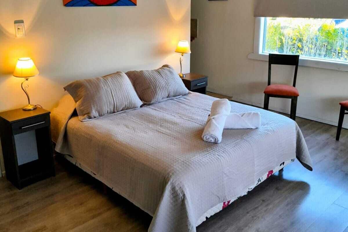 A bedroom with a bed, two bedside tables, a window, and a painting on the wall.