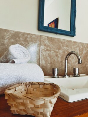 Un baño con lavamanos, espejo, toalla y una cesta de mimbre.