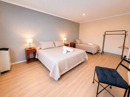 Ein Hotelzimmer mit einem großen Bett, zwei Nachttischen mit Lampen, einem Sessel und einem Metallregal.