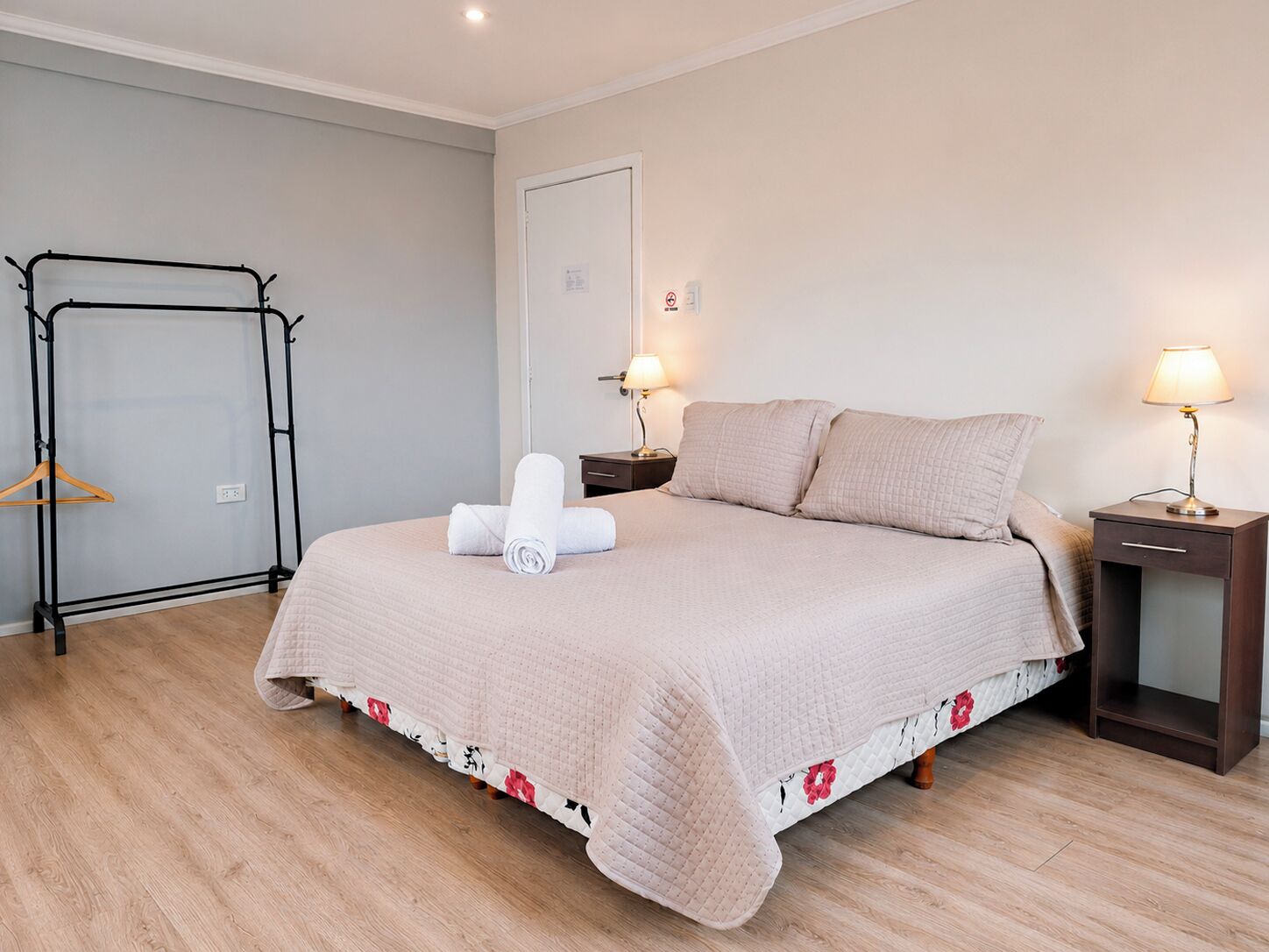 A neatly made bed with a quilted cover, a bedside table with a lamp, and a wooden floor.