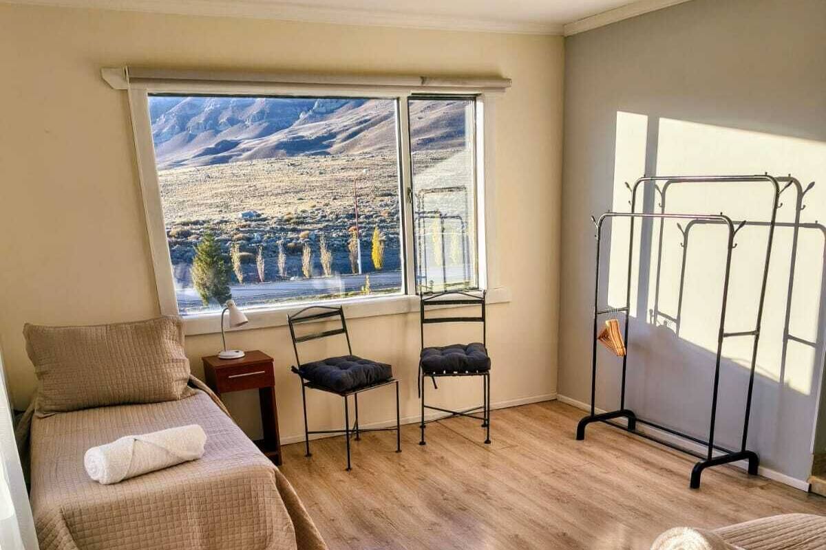 A hotel room with two beds, a window with a mountain view, a chair, and a metal drying rack.