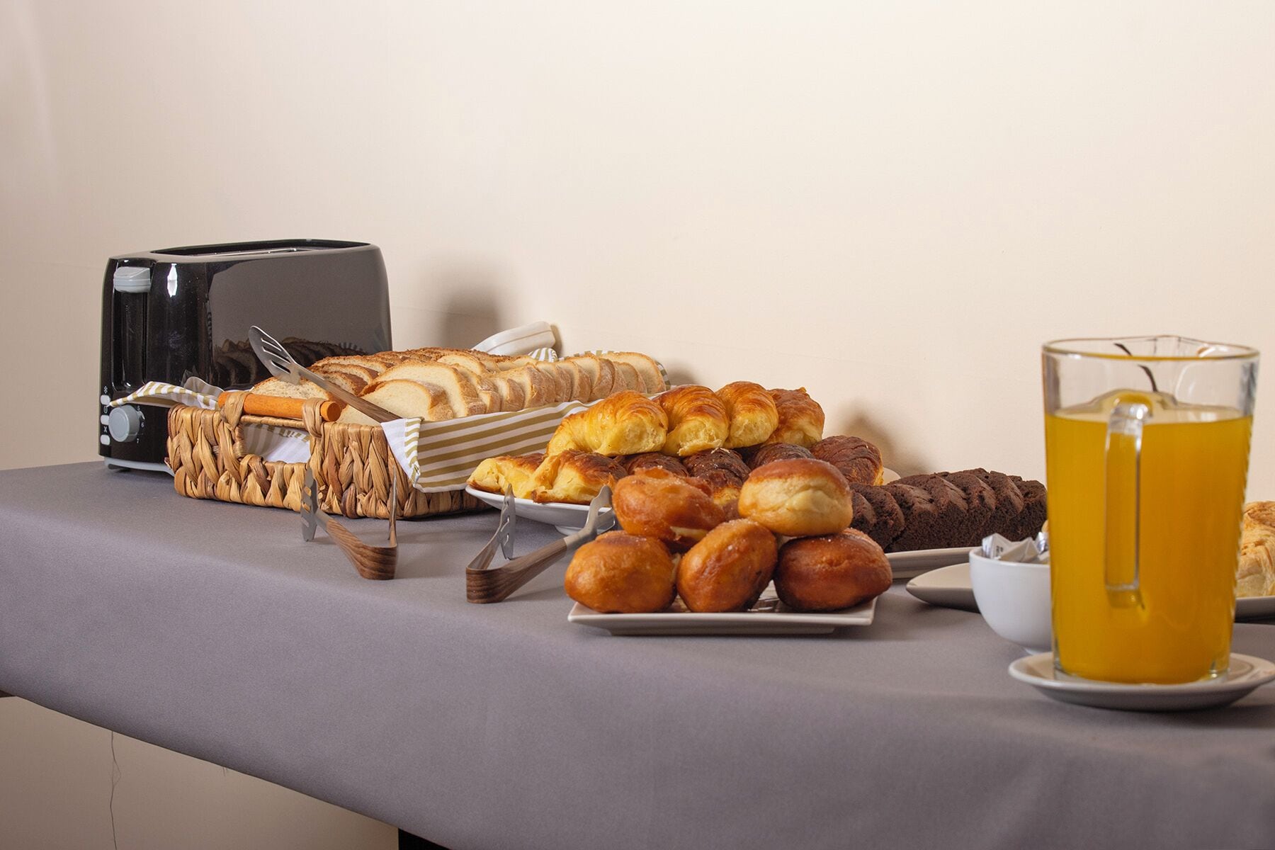 A breakfast buffet with bread, pastries, and a glass of orange juice.