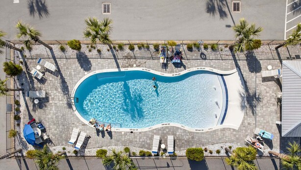 Eine Vogelperspektive auf einen Swimmingpool mit Liegestühlen und Palmen.