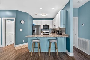 A modern kitchen with white cabinets, a granite countertop, and two bar stools. - Hidden Lake 622 – Coastal Luxury Condo with Community Pool (Santa Rosa Beach)