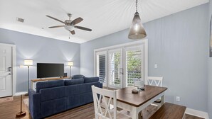 Ein Wohnzimmer mit Sofa, Esstisch, Stühlen, Deckenventilator und Fernseher.