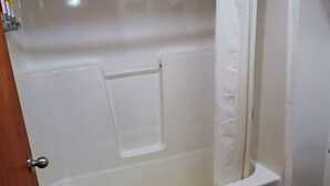 Une baignoire avec un rideau de douche, une serviette et une porte en bois.