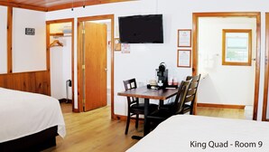 Une chambre d’hôtel comprenant un lit, une table à manger avec des chaises, une machine à café, un téléviseur fixé au mur et une porte donnant sur une autre pièce.