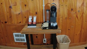Un coin café équipé d’une machine à café Keurig, de gobelets jetables et d’une poubelle, dans une pièce aux murs en bois.