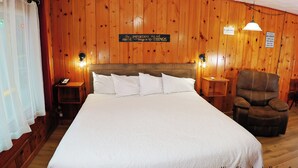 Une chambre de catégorie « King Standard », dotée d’un grand lit, de murs en bois, de deux lampes de chevet, d’une chaise et d’un panneau affichant une citation inspirante.