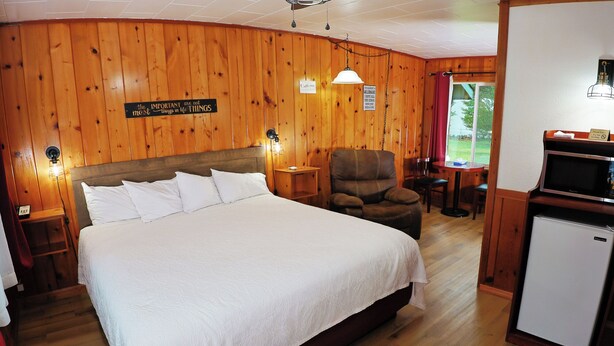 Une chambre de catégorie « King Standard » avec un grand lit, des murs en bois, une chaise, une table et un réfrigérateur.