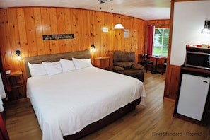 A King Standard room with a large bed, wooden walls, a chair, a table, and a refrigerator. - King Standard: Rustic Knotty Pine Retreat w/ Recliner & Nature Vibes (Florence)