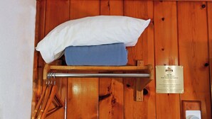 Un mur en bois, un coussin blanc et une serviette bleue sont posés sur un étagère en métal. On peut voir une pancarte avec un message.