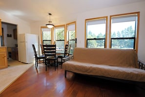 A living room with a sofa, chairs, a dining table, and a kitchen area with a refrigerator.