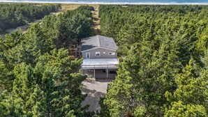 A house surrounded by dense forest with a clear view of the ocean.