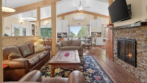 A spacious living area with a fireplace, wooden beams, a television, and a view to the outside.