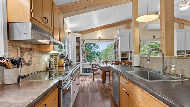 A kitchen with wooden cabinets, stainless steel appliances, a central island, and a view of greenery outside.