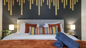 A hotel room with a bed, striped pillows, a headboard, bedside lamps, and a wall with wooden slats. - Beach + Lake Access | AC, Game Room, Fire Pit (Albrightsville)