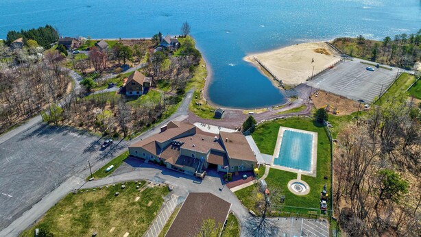 An aerial view of a lakeside property with a swimming pool, a large building, and a parking lot. - Beach + Lake Access | AC, Game Room, Fire Pit (Albrightsville)