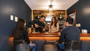 A bar area with a bartender, three seated customers, and a wooden wall with a hanging light fixture. - Beach + Lake Access | AC, Game Room, Fire Pit (Albrightsville)