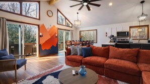 A spacious living room with a large sofa, a coffee table, and a dining area with chairs. - Beach + Lake Access | AC, Game Room, Fire Pit (Albrightsville)