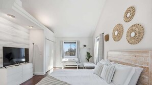 Ein modernes Schlafzimmer mit einem großen Bett, einem Fernseher, einem Schreibtisch und einem Fenster.
