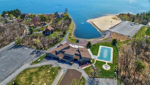 Luftaufnahme eines Sees mit einem Grundstück, das einen Swimmingpool, ein großes Gebäude und einen Parkplatz bietet.