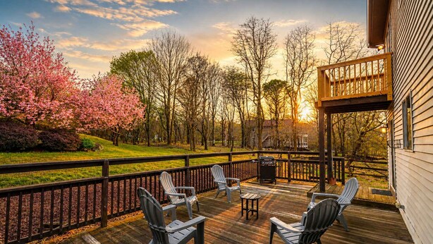 Eine Terrasse mit Sitzgelegenheiten, einem Grill und Blick auf Bäume und einen Sonnenuntergang.