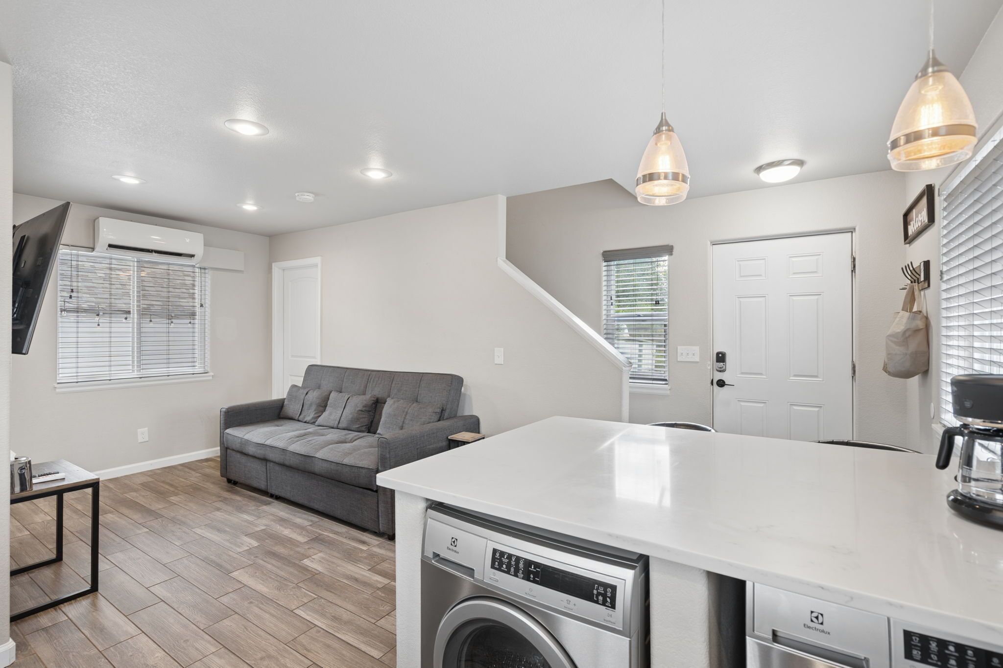 A compact kitchen with a built-in dishwasher, a grey sofa, and a white countertop.