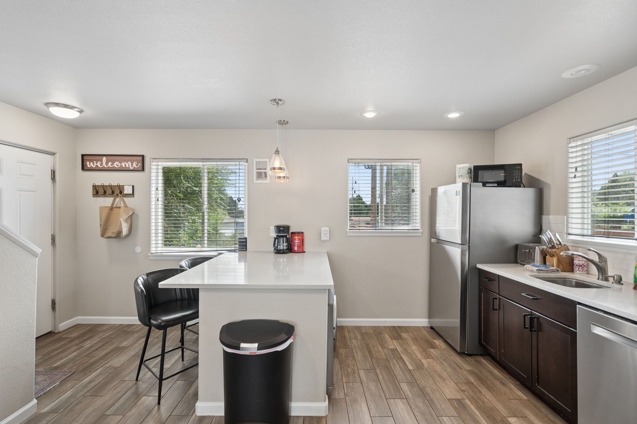 A modern kitchen with a central island, bar stools, a refrigerator, and a microwave.