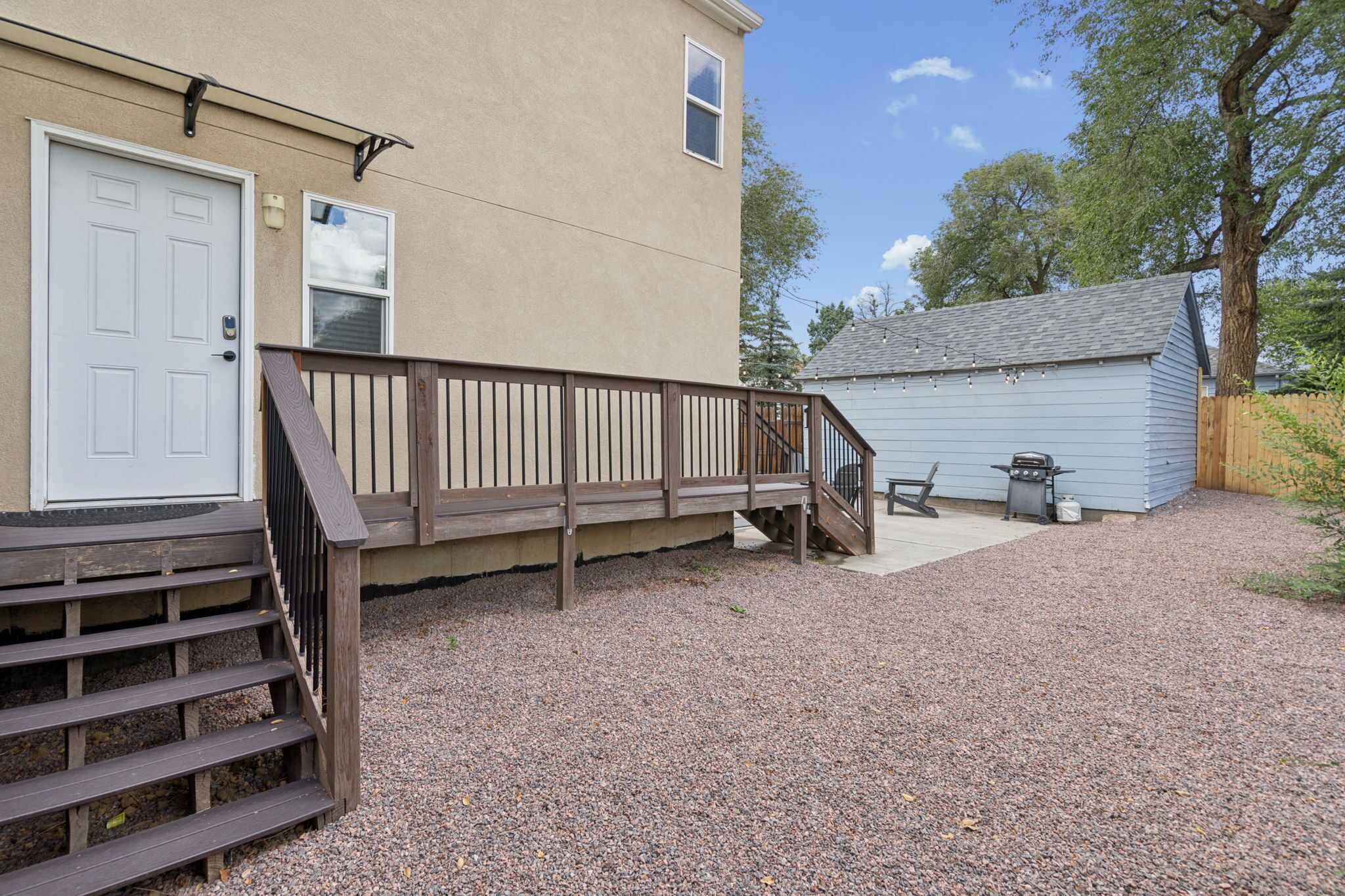 A building with a wooden deck, a door, and a small shed with a grill.