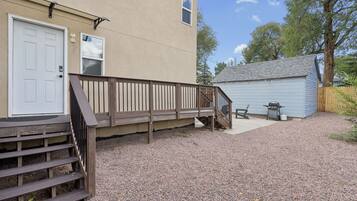 A building with a wooden deck, a door, and a small shed with a grill.