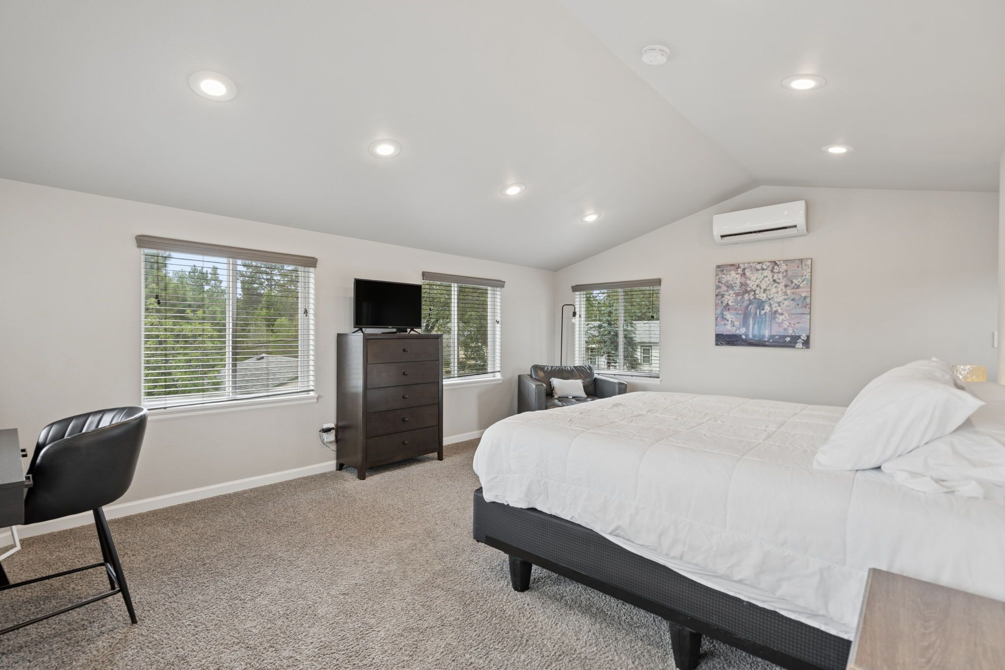 A bedroom with a bed, dresser, TV, and a desk with a chair.
