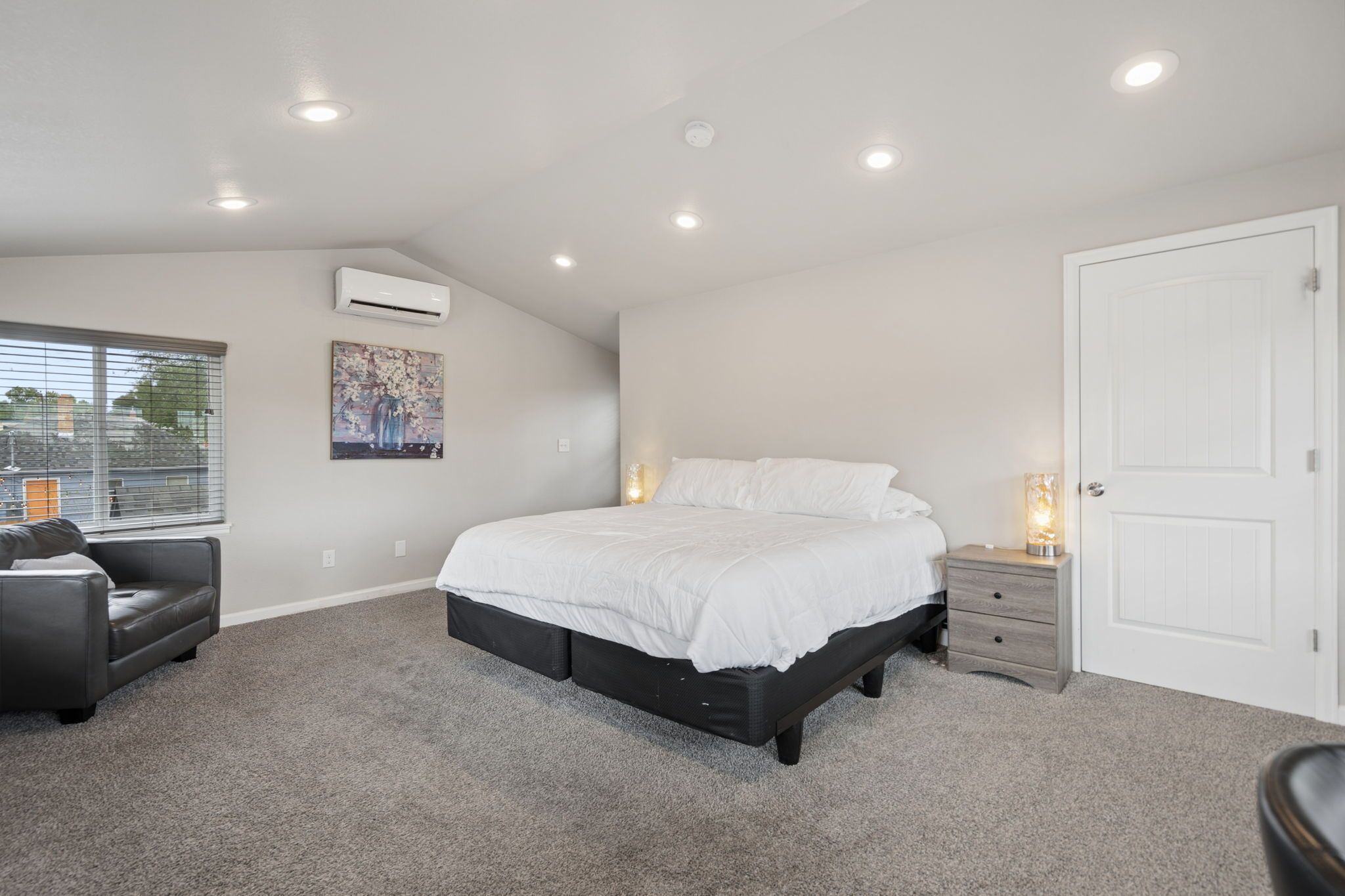 Un dormitorio con cama, mesita de noche, cómoda, ventana con persianas y unidad de aire acondicionado.
