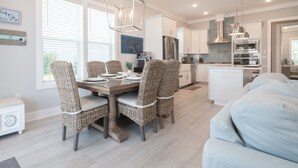 Een moderne keuken met witte kasten, een centraal eiland en een eethoek met rieten stoelen.