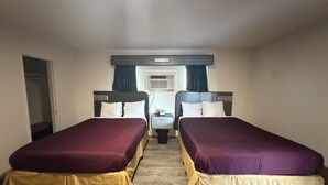 A hotel room with two beds, a small table, an air conditioning unit, and a window with curtains. - Townhouse Motel (Tracy)