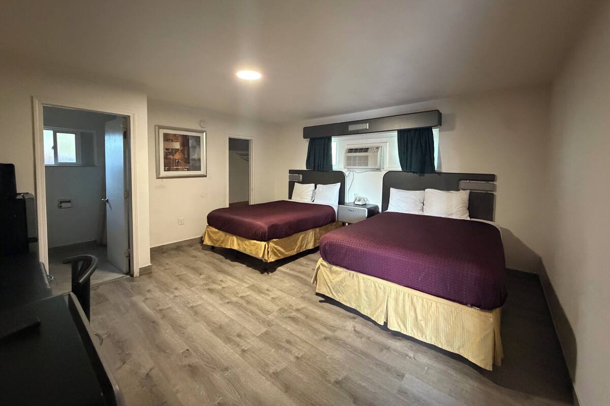 Habitación de hotel con dos camas, un escritorio, una silla, un ventanal y un aire acondicionado.