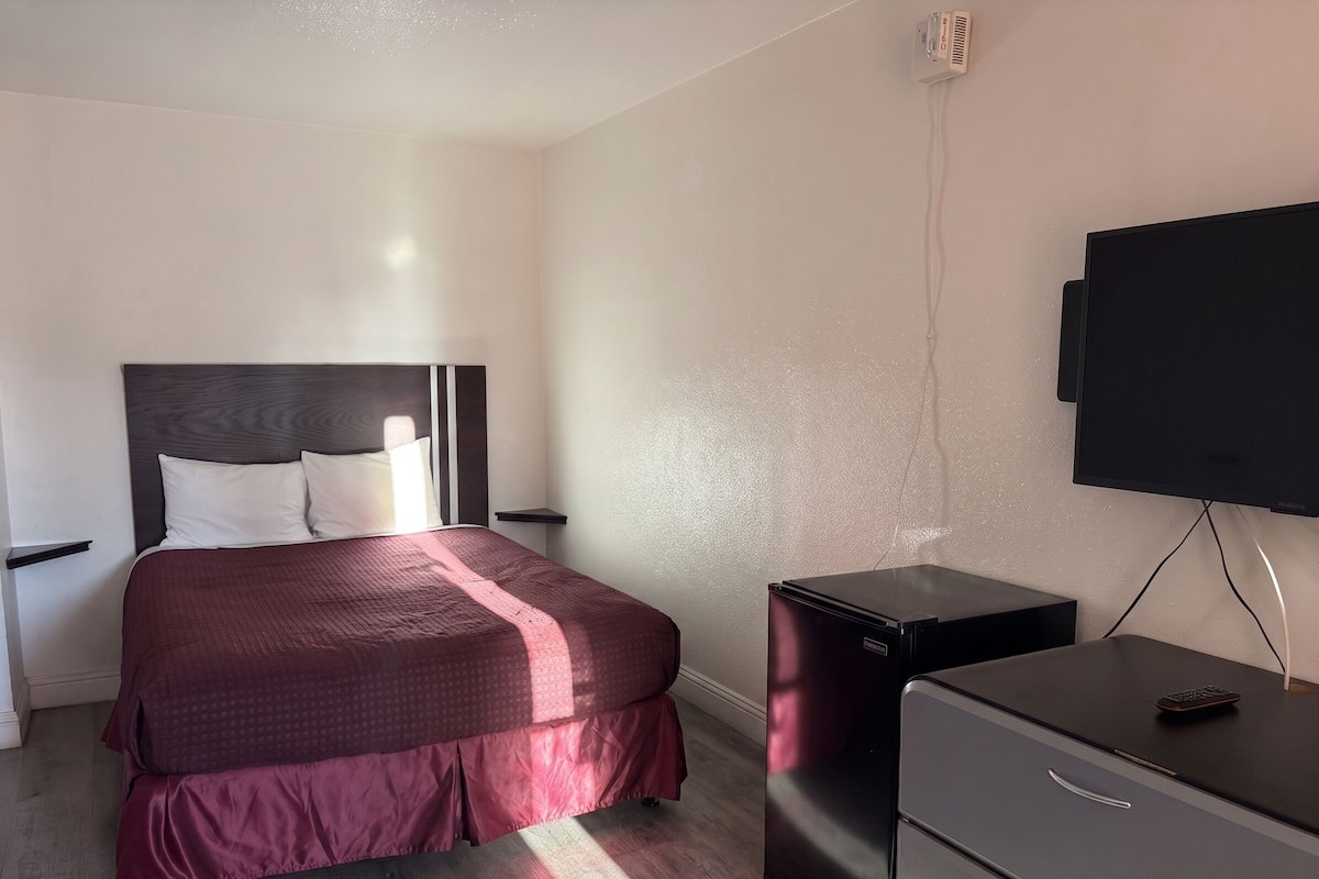Una habitación de hotel con cama, escritorio, televisor y un pequeño refrigerador.