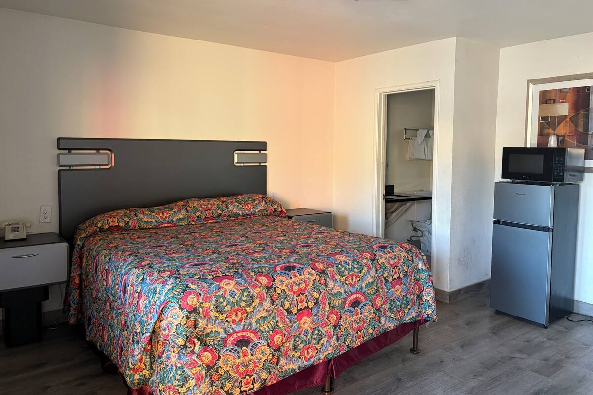Un dormitorio con cama, mesita de noche, cómoda, microondas y refrigerador.