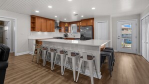 Una cocina moderna con una isla grande, taburetes de bar, armarios de madera y vistas a través de la puerta.