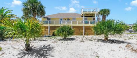 A beachfront property with a wooden deck, palm trees, and a building with a balcony.