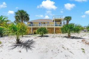 A beachfront property with a wooden deck, palm trees, and a building with a balcony.