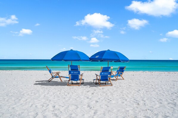 A beach with two blue umbrellas and four blue lounge chairs.
